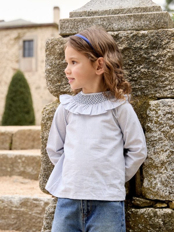 Blusa de niña a finas rayas azul cielo y blanco con cuello con nido de abeja, llevada por una niña pequeña