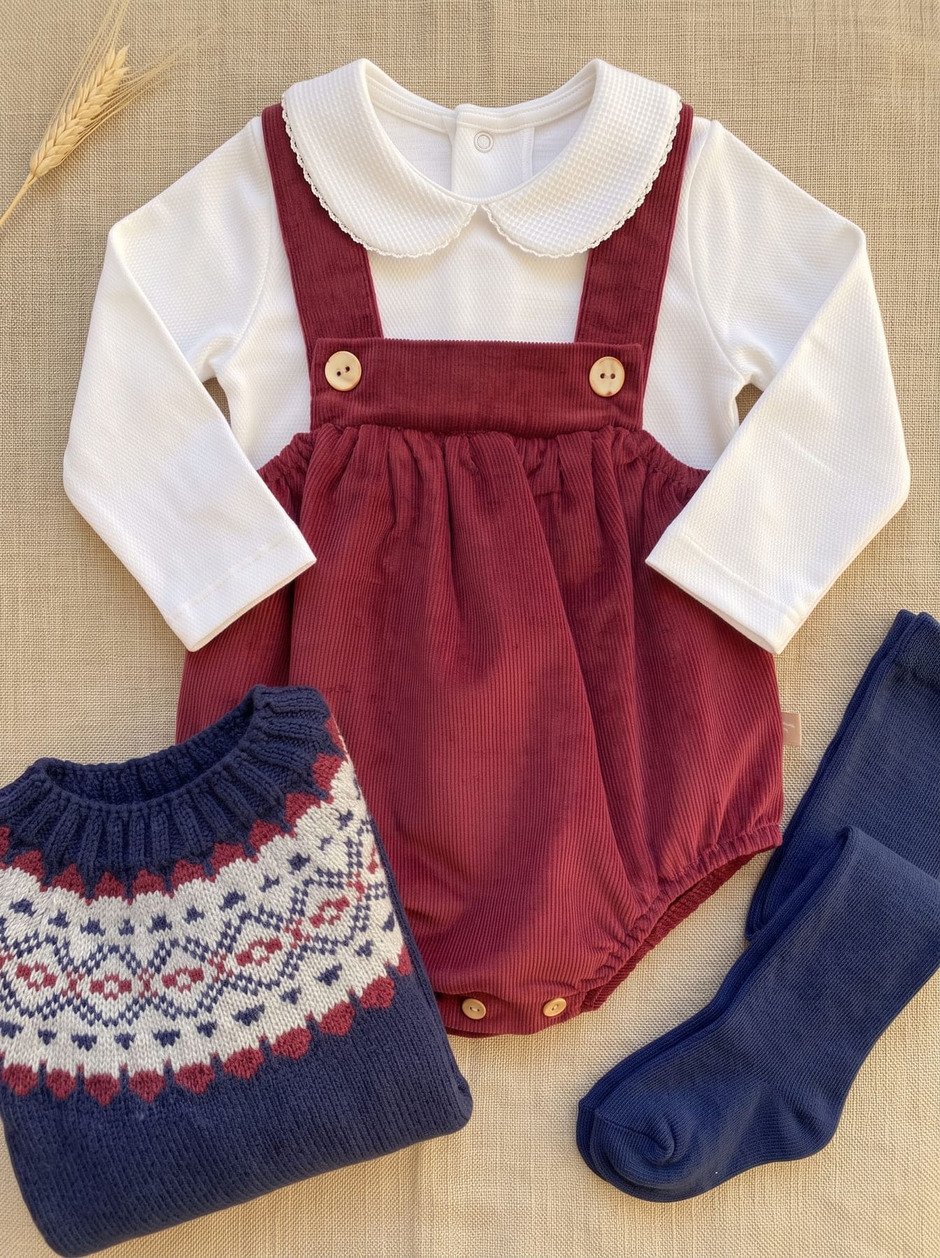 Detail of the baby boy look with burgundy romper, white blouse and patterned cardigan
