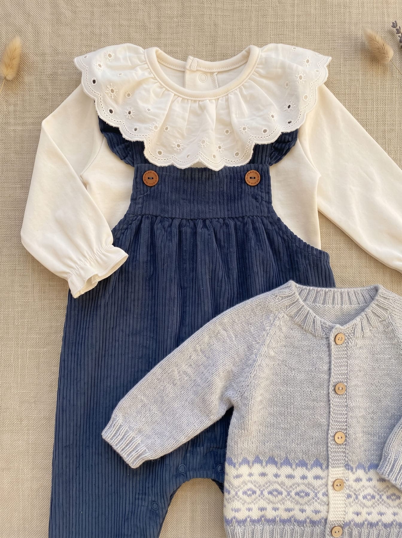 Détail du look fille avec salopette bleu marine, blouse blanche à col festonné et cardigan gris