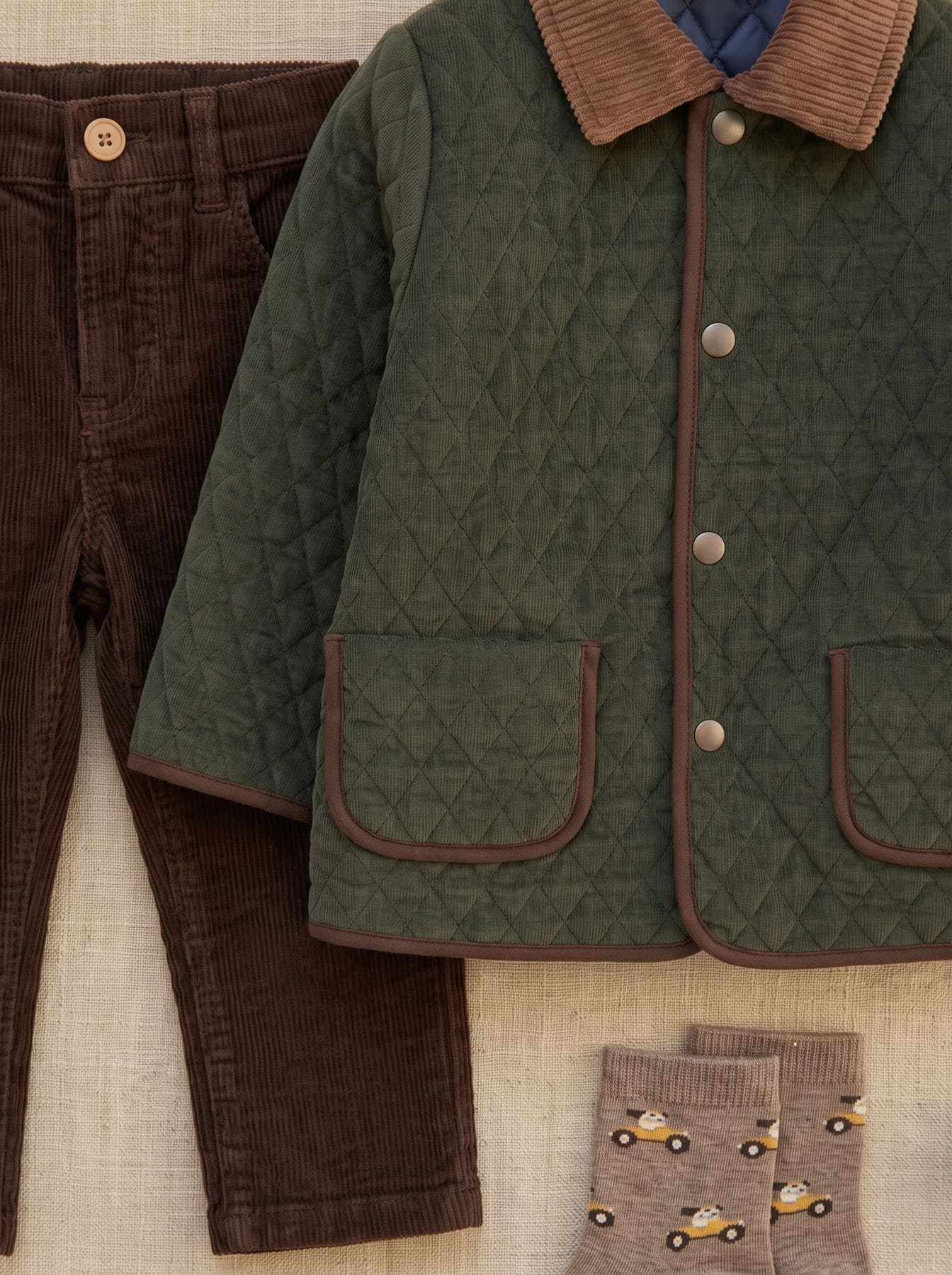 Détail de la tenue garçon avec veste matelassée vert foncé, pantalon marron et chaussettes à motifs