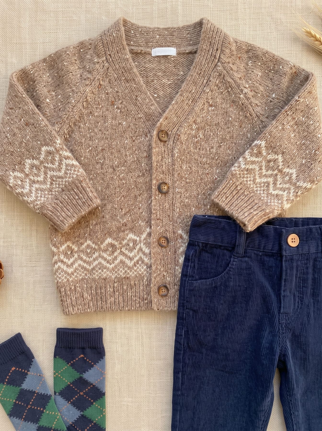 Détail du look garçon avec cardigan beige à motifs, pantalon bleu marine et chaussettes à carreaux